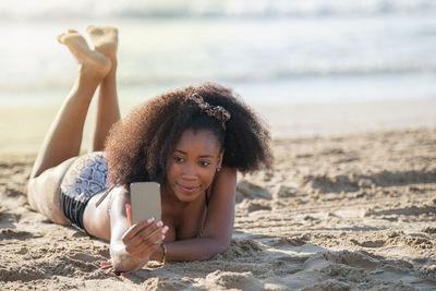 Young woman taking selfie while lying on beach