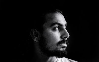 Portrait of young man looking away against black background