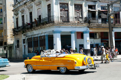 People sitting in yellow car on road against building