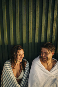 Smiling man and woman wearing towel while talking to each other during sunset