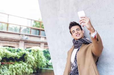 Young man taking selfie from mobile phone by wall