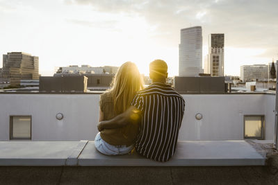 Rear view of boyfriend and girlfriend sitting on terrace and looking at buildings in city