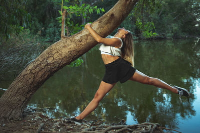 Full length of woman exercising by tree and lake