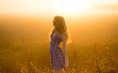 Woman standing on field against sky during sunset