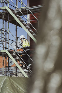 Full length of female building contractor talking on smart phone while moving up on steps at construction site