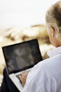 Over the shoulder view of senior man using laptop outdoors