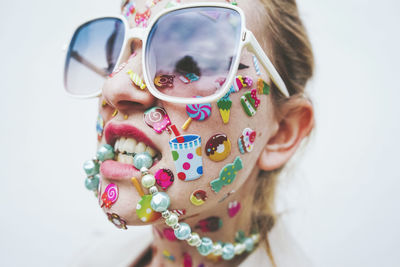 Woman with multi colored stickers on face biting necklace in front of white background