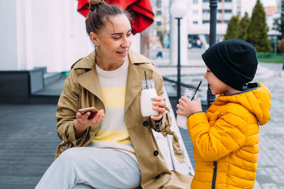 Young mom and son have fun and drink milkshake outdoors.