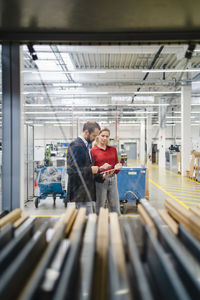 Business colleagues discussing over tablet pc standing in production hall