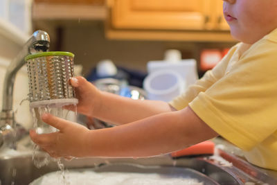 Boy washing container at kitchen sink