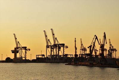 Cranes at commercial dock against clear sky during sunset