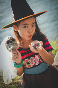 Portrait of girl wearing witch hat holding skull and crystal ball