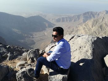 Side view of young man sitting on mountain