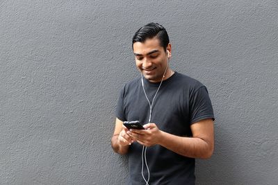 Young man looking away while using mobile phone against wall