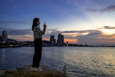 Female teenager wearing n95 mask while talking pictures of sunset at a beach in sriracha, thailand