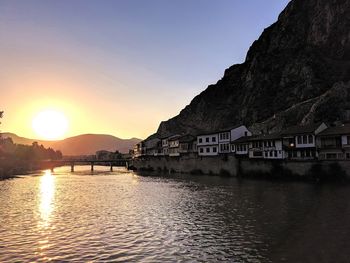 Scenic view of lake by buildings against sky during sunset