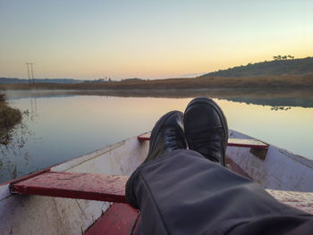 Man foot on traditional wood boat at calm lake with dramatic sunrise colorful sky reflection