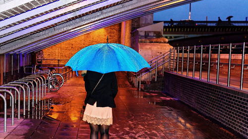 Rear view of woman with umbrella in building during rainy season