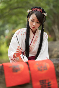 Young woman in chinese traditional dress writing with a brush pen