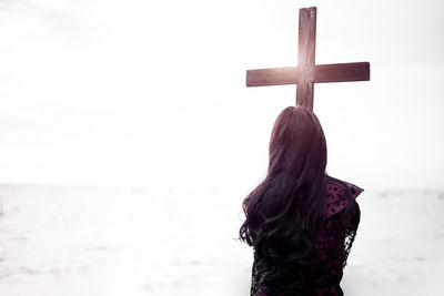 Rear view of woman standing by religious cross against sea and sky