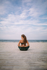 Young woman sitting on shore at beach against sky