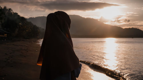 Woman standing on shore against sky during sunset