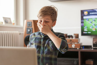 Surprised boy covering his mouth while watching something on a computer at home.