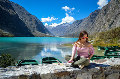 Full length of woman sitting by lake against mountains