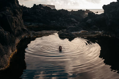 From above of female swimming in clean lake surrounded by rocky cliffs near sea and looking at camera