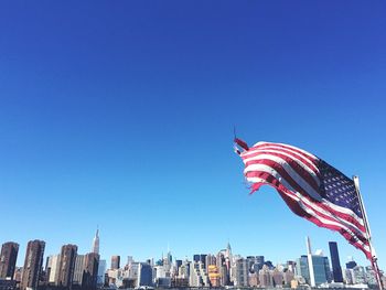 Low angle view of torn american flag blowing against clear sky in city