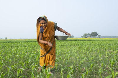 Woman farmer working in field holding fertilizer in basket