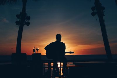 Silhouette man sitting by sea against sky during sunset