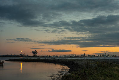 Scenic view of river by buildings against sky during sunset