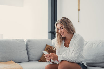 Young woman using mobile phone while sitting on sofa at home