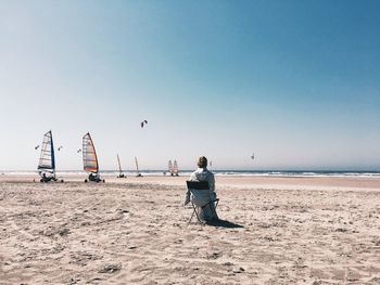 Rear view of person sitting on chair at beach against clear sky during sunny day