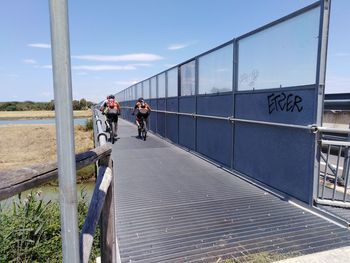 People riding bicycle on bridge against sky