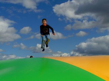 Full length of smiling boy jumping on trampoline against sky