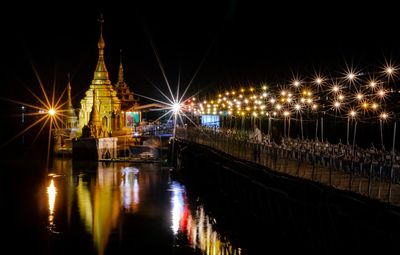 Illuminated city by river against sky at night