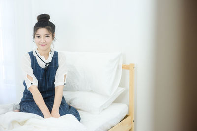 Smiling young woman sitting on bed at home