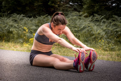 Full length of woman exercising while sitting on road