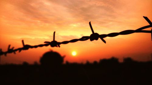 Barbed wire against sky at sunset