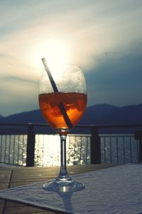 Wineglass on table by sea against sky during sunset