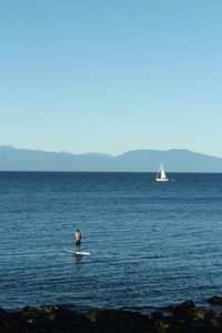 Man paddleboarding in sea against clear sky