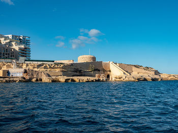 Buildings by sea against blue sky