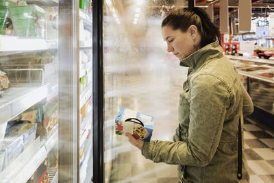 Side view of woman reading food label at refrigerated section