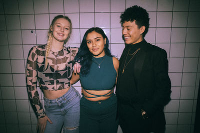 Portrait of happy young woman standing with arms around non-binary friend against white wall