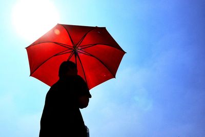 Low angle view of person holding red umbrella against blue sky