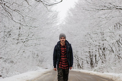 Portrait of young man standing on road amidst frozen trees on field