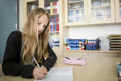 Girl writing in book on desk at classroom