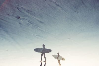 People with surfboard reflected on wet beach